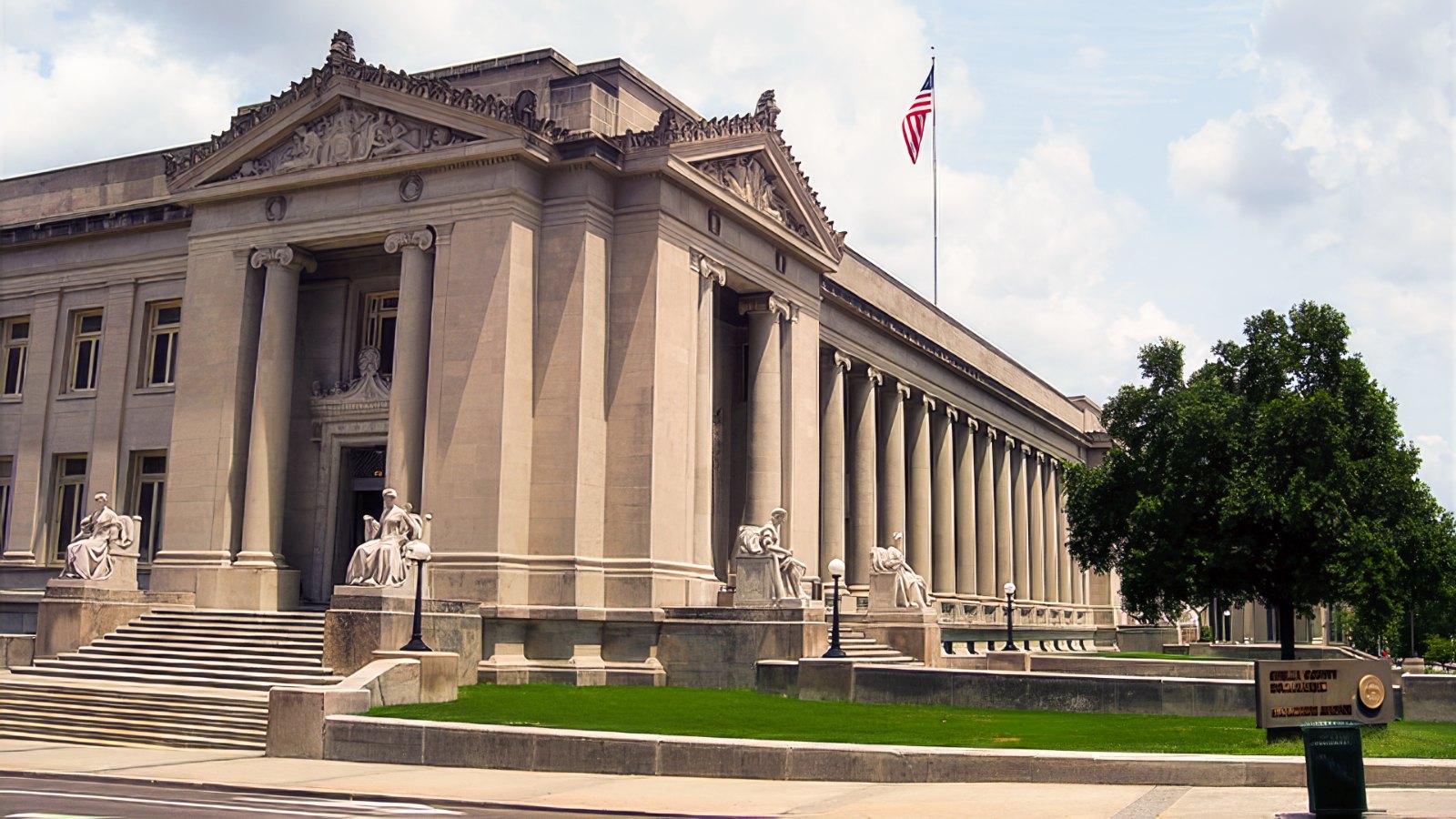 The Shelby County Courthouse on Adams Avenue in downtown Memphis, a neoclassical limestone building with columns and seated allegorical statues along its steps.